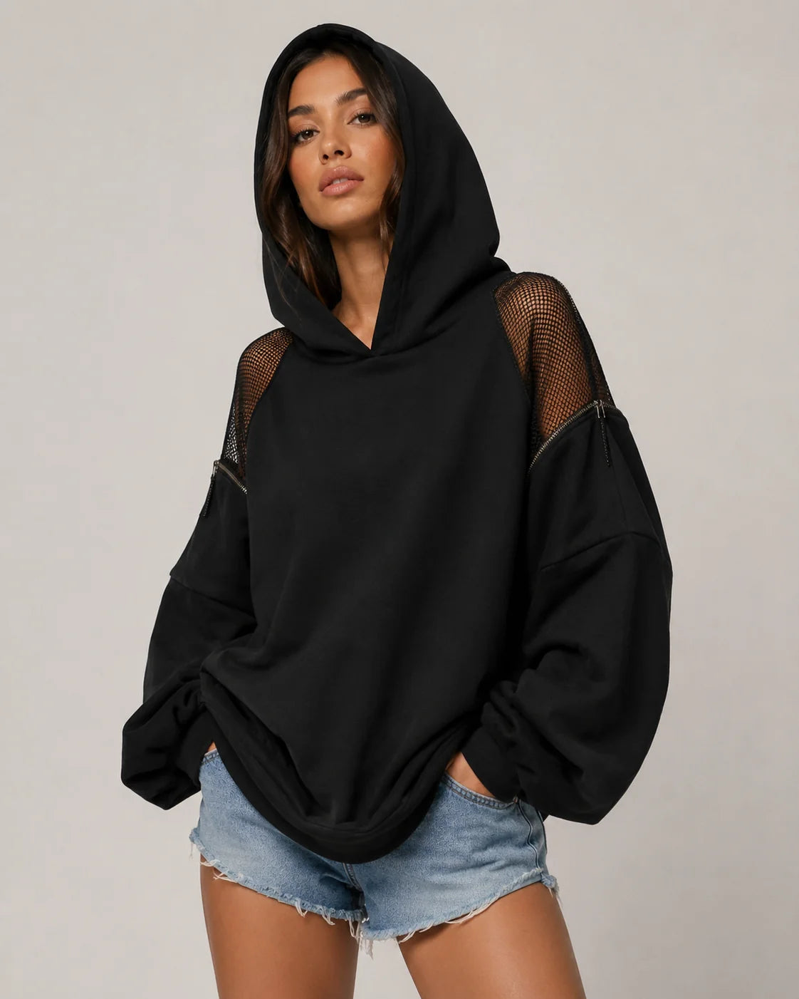 Woman in a black oversized hoodie with mesh details on the shoulders, hood and denim shorts