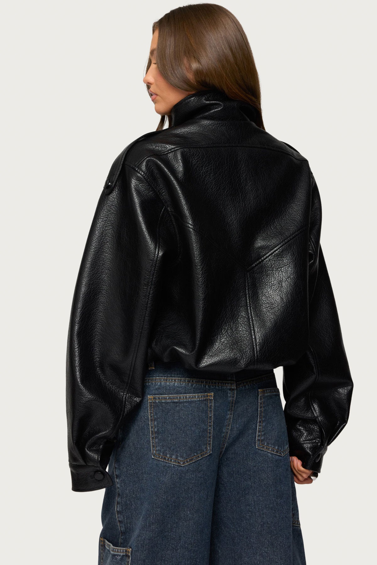 Back view of a black oversized faux leather jacket with shoulder tabs, yoke seams, elastic hem and snaps on the sleeves